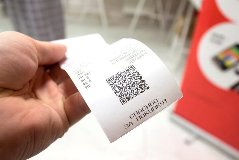 Кассовый чек с QR-кодом в руке у кассы